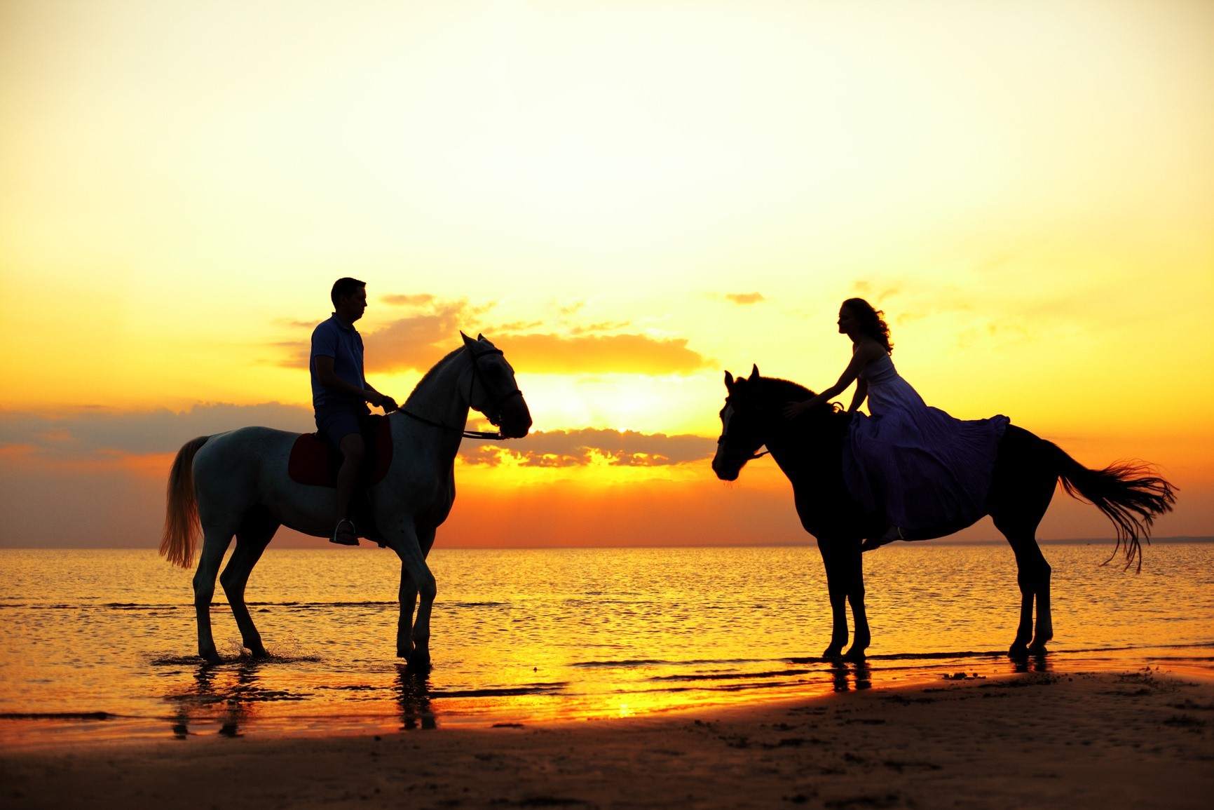 Horseback Riding - Two riders on horseback at sunset on the beach. Lovers ride horse